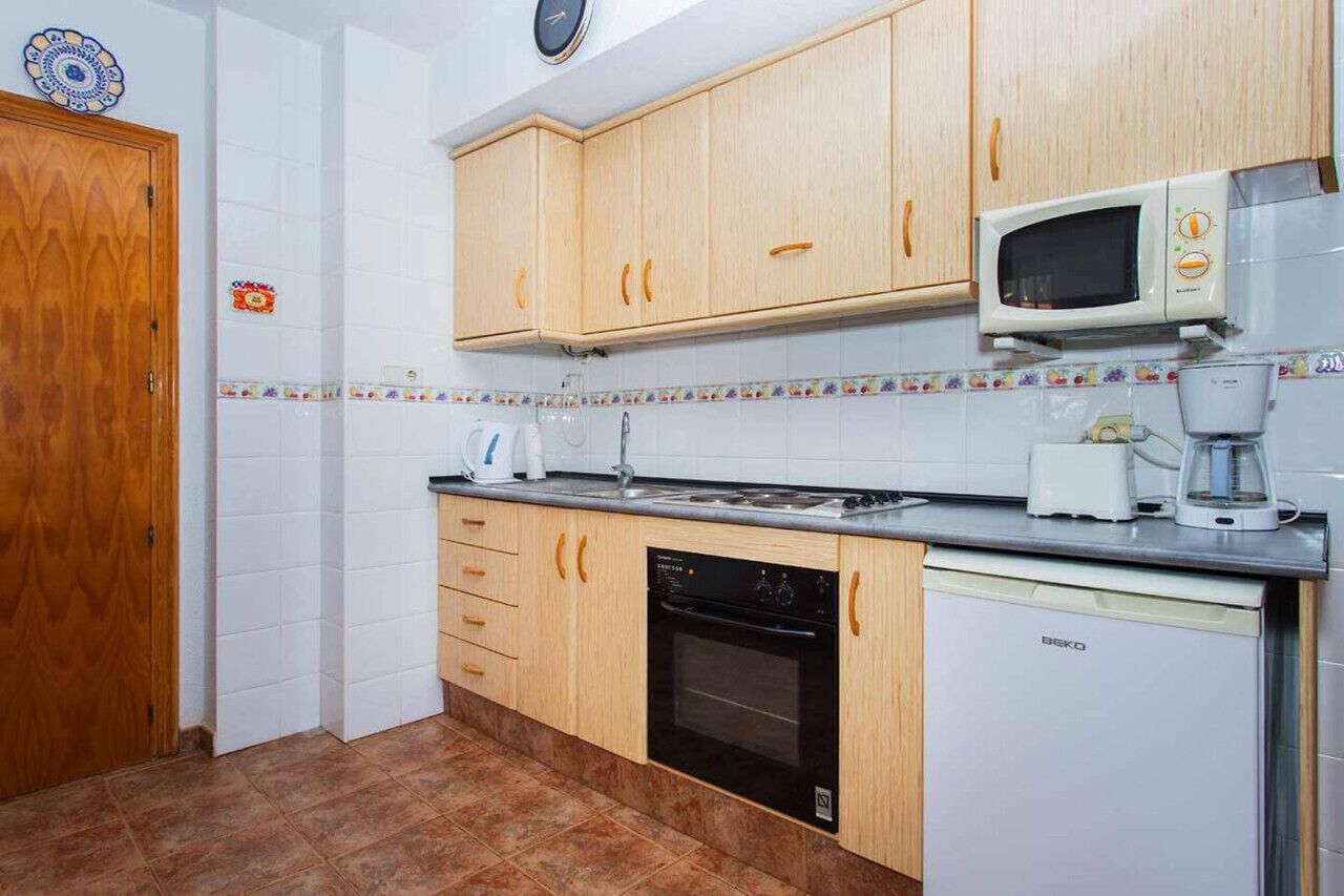 Una cocina con armarios de madera, microondas, lavavajillas y cafetera.