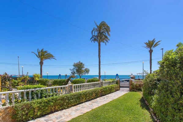 A pathway leading to a gated area with a view of the sea and palm trees.