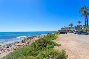 Una carretera costanera amb un senyal de 'NAUTILUS', una platja amb palmeres i terreny rocos.