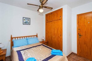 A bedroom with a bed, wooden wardrobe, and a ceiling fan.