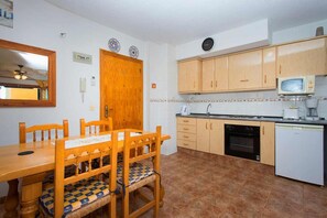 A compact kitchen with wooden cabinets, a microwave, a dishwasher, and a dining table with chairs.