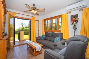 Una sala de estar con un sofá, un sillón y un ventilador de techo. Hay una puerta corrediza de vidrio que da a un balcón.