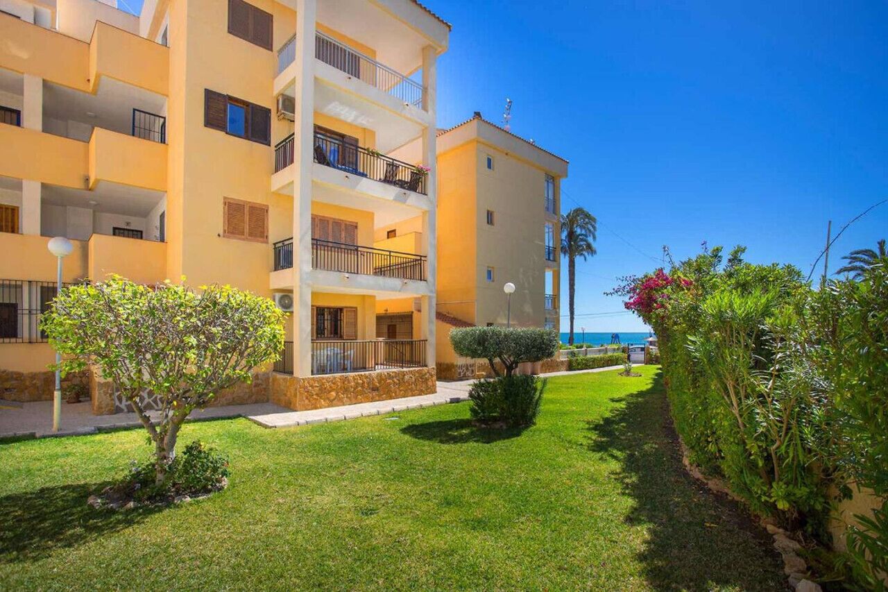 Un edificio de varios pisos con balcones, un césped cuidado y una vista despejada del mar.