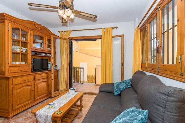 A living room with a sofa, wooden cabinets, a ceiling fan, and a view through a glass door.