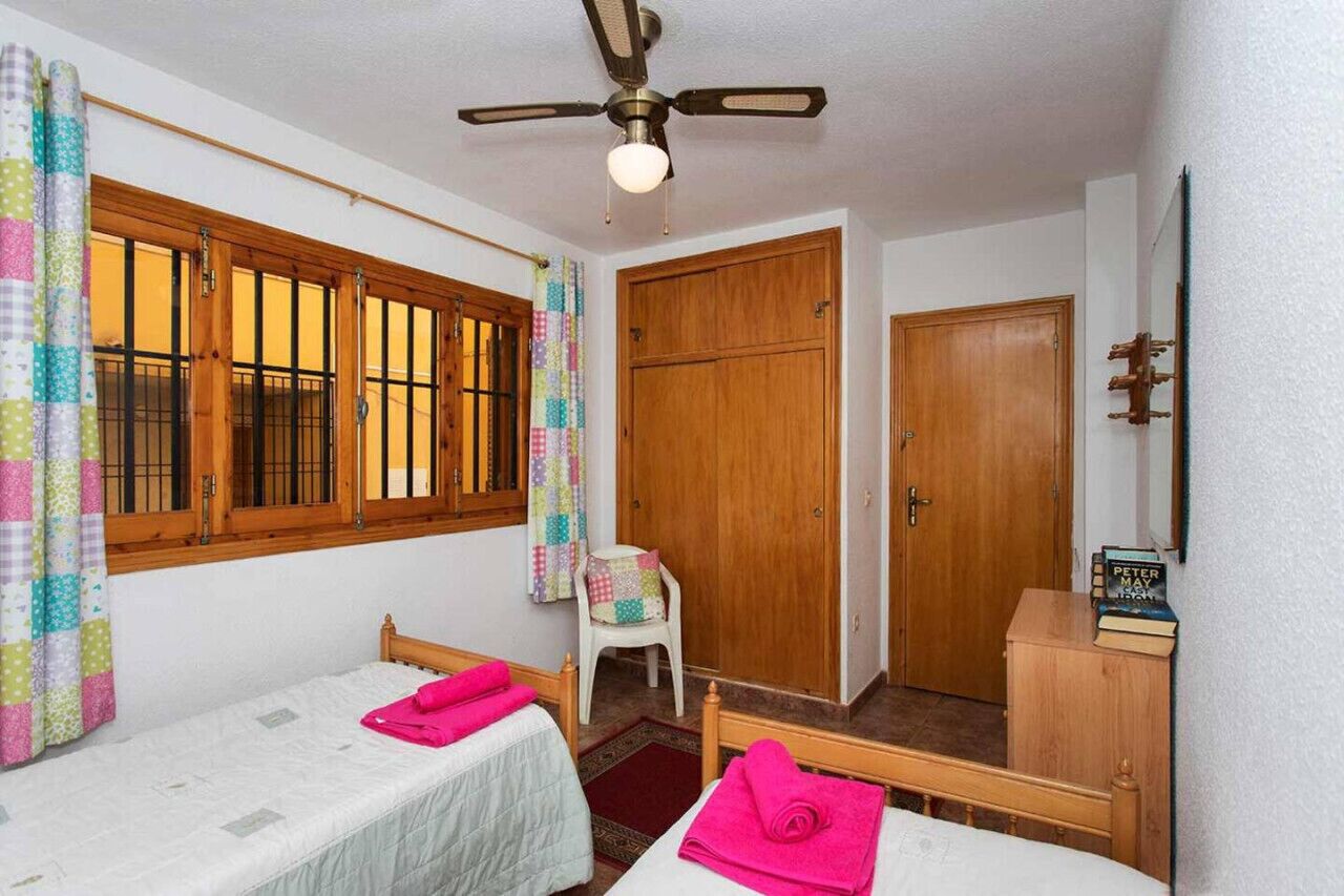 Una habitación con dos camas, un armario de madera, un ventilador de techo y una ventana con cortinas.