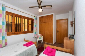 A room with two beds, a wooden wardrobe, a ceiling fan, and a window with curtains.