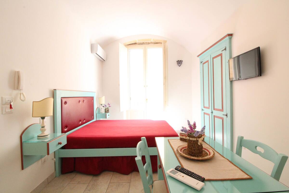 Ein Schlafzimmer mit Bett, Schreibtisch, Stuhl, Fernseher und Fenster.