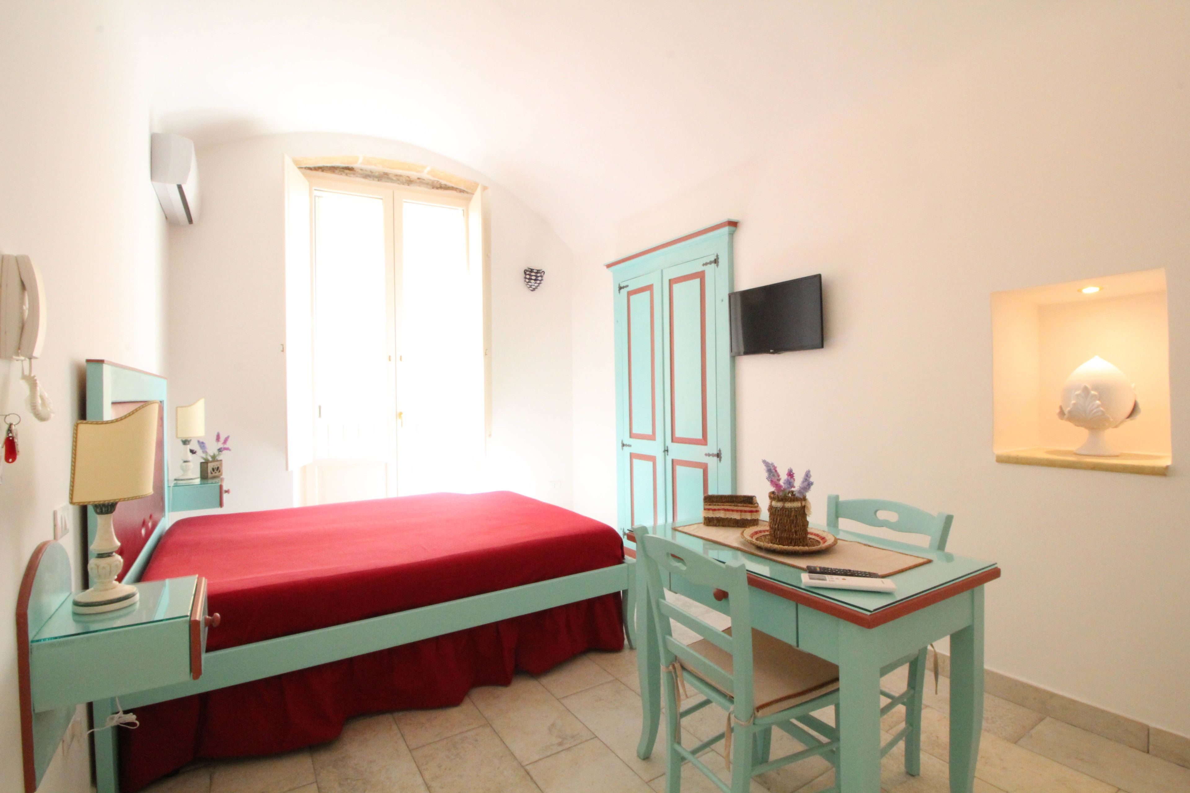 Un dormitorio con cama, escritorio, silla, televisor y ventana.