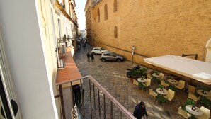 Une rue étroite avec un café sur le côté droit, doté d’une terrasse et d’un grand parasol.