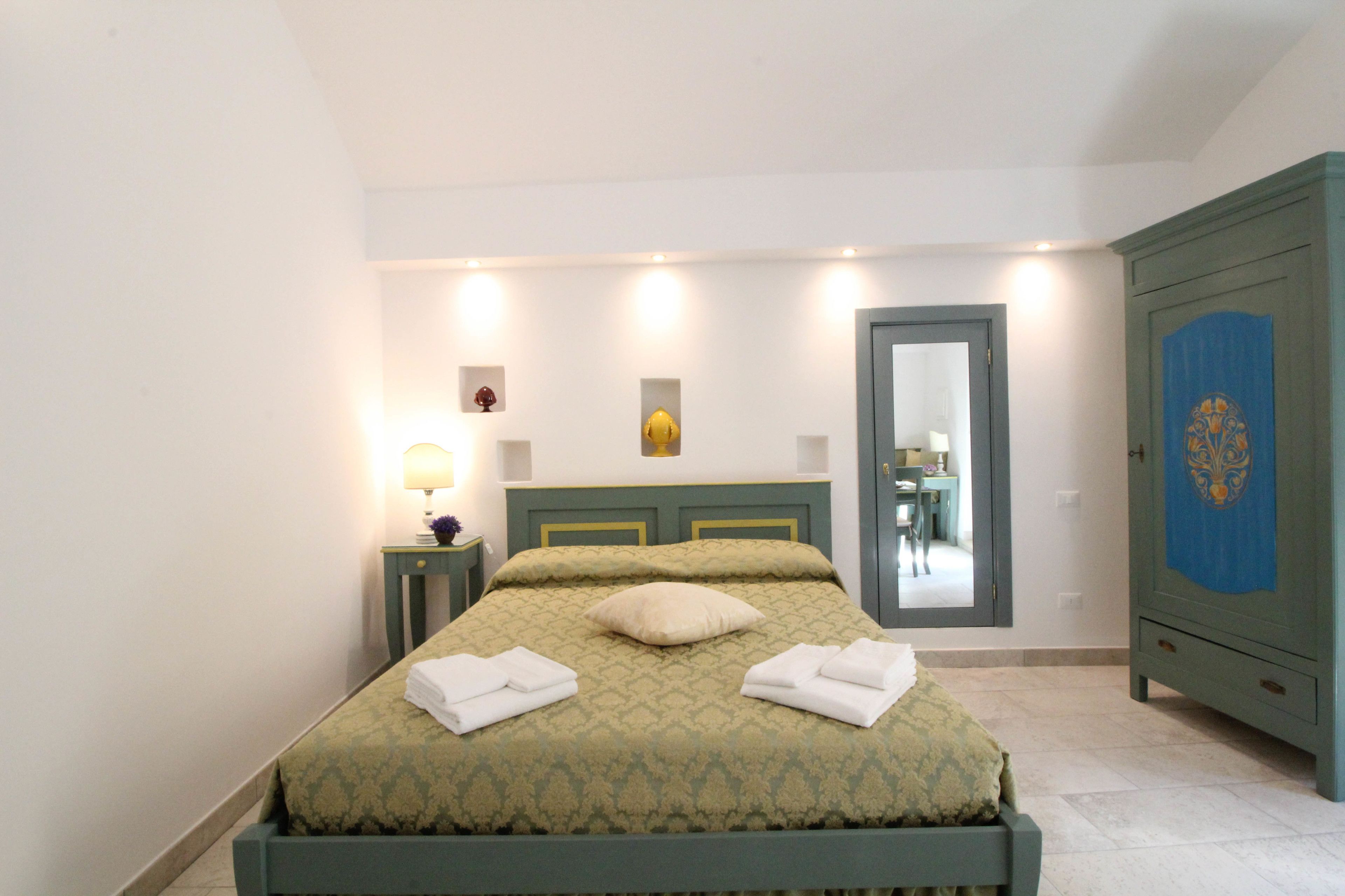 A neatly made bed with a patterned bedspread and pillows, a bedside table with a lamp, and a wardrobe with a decorative panel.