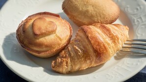Une assiette avec trois viennoiseries : un croissant, un pain rond et un petit pain rond.