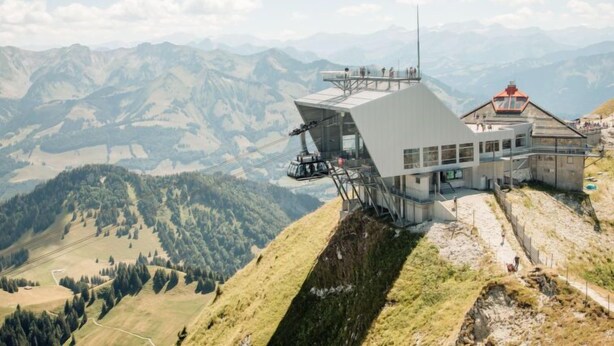 Un chalet de montagne au design moderne, doté d’une grande façade vitrée et d’une tour d’observation surmontée d’un toit rouge.
