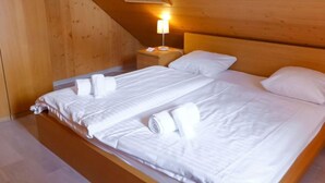 Un lit simple avec du linge de lit blanc et des oreillers, une table de chevet avec une lampe, et des panneaux de bois sur les murs.