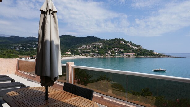 A balcony with a table and chairs, a view of a coastal town, and a boat on the water. - Résidence les Pavillons du Golfe (Conca)