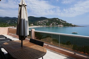 A balcony with a table and chairs, a view of a coastal town, and a boat on the water. - Résidence les Pavillons du Golfe (Conca)