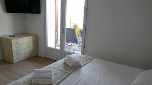 A bedroom with a bed, a wooden dresser, a television, and a sliding glass door leading to an outdoor area. - Résidence les Pavillons du Golfe (Conca)