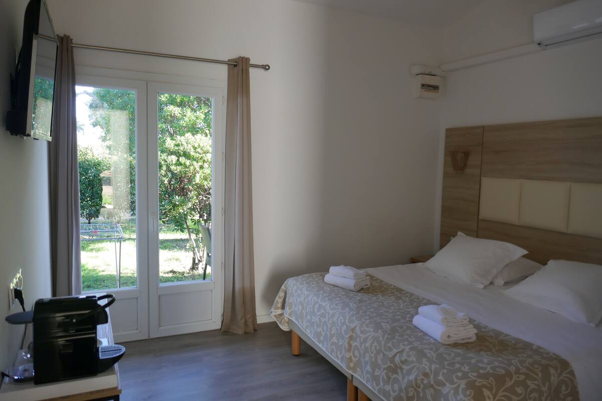 A hotel room with a bed, a coffee machine, and a view of the outdoors through a glass door.