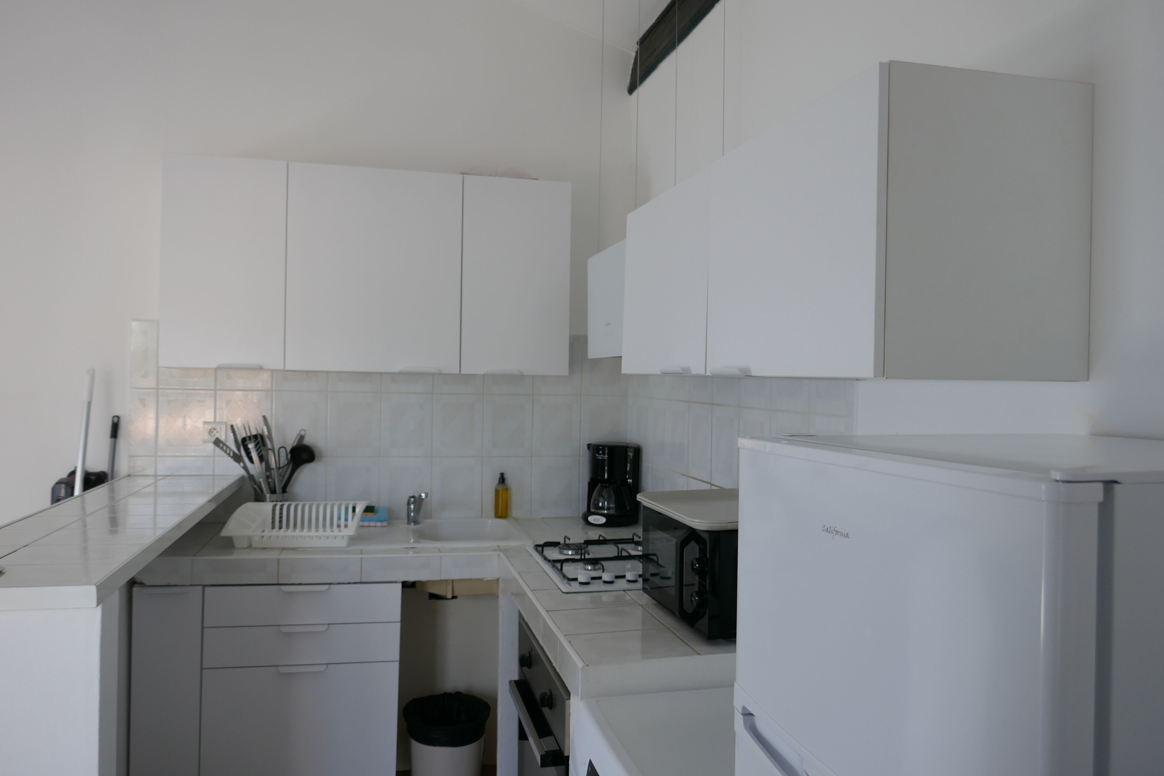A modern kitchen with white cabinets, a countertop, a stove, a microwave, and a trash bin.