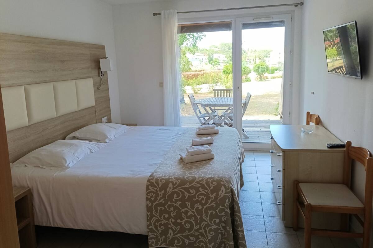 A hotel room with a bed, a desk, a chair, a TV, and a view of the outside.