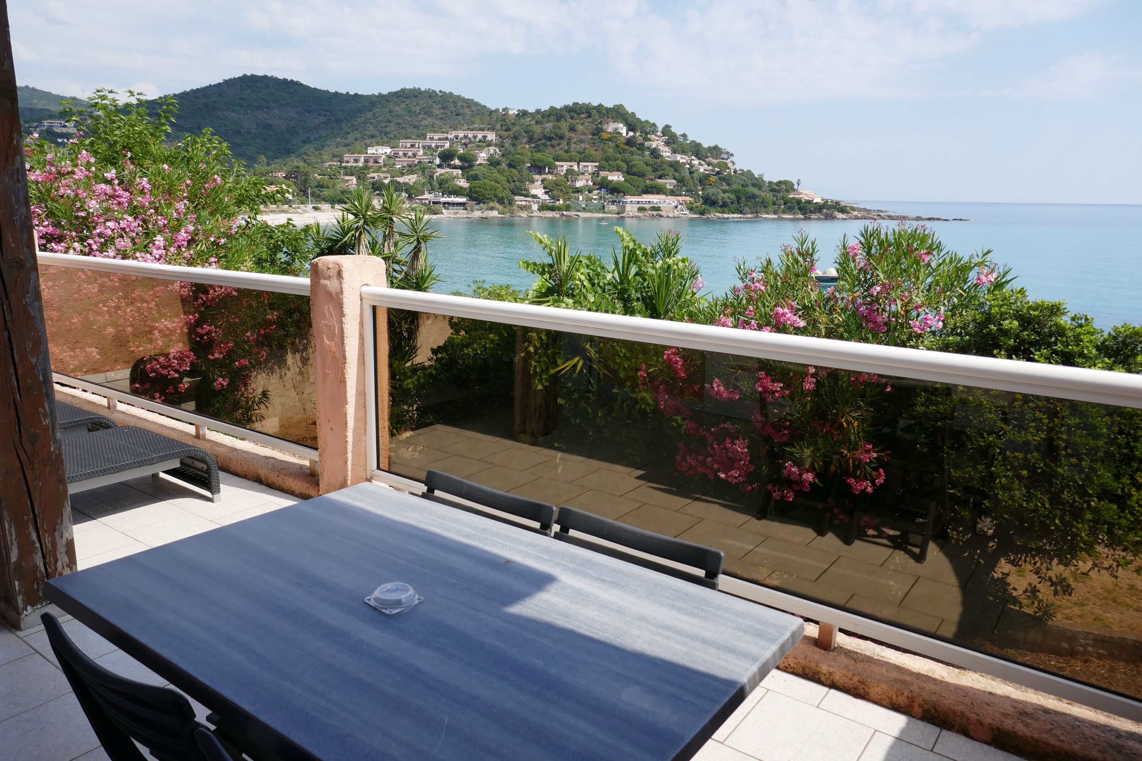 A balcony with a table and chairs, overlooking a coastal town with buildings on a hillside.
