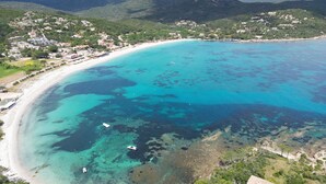 An aerial view of a coastal area with a clear turquoise sea, a sandy beach, and a town with buildings on a hillside. - Résidence les Pavillons du Golfe (Conca)