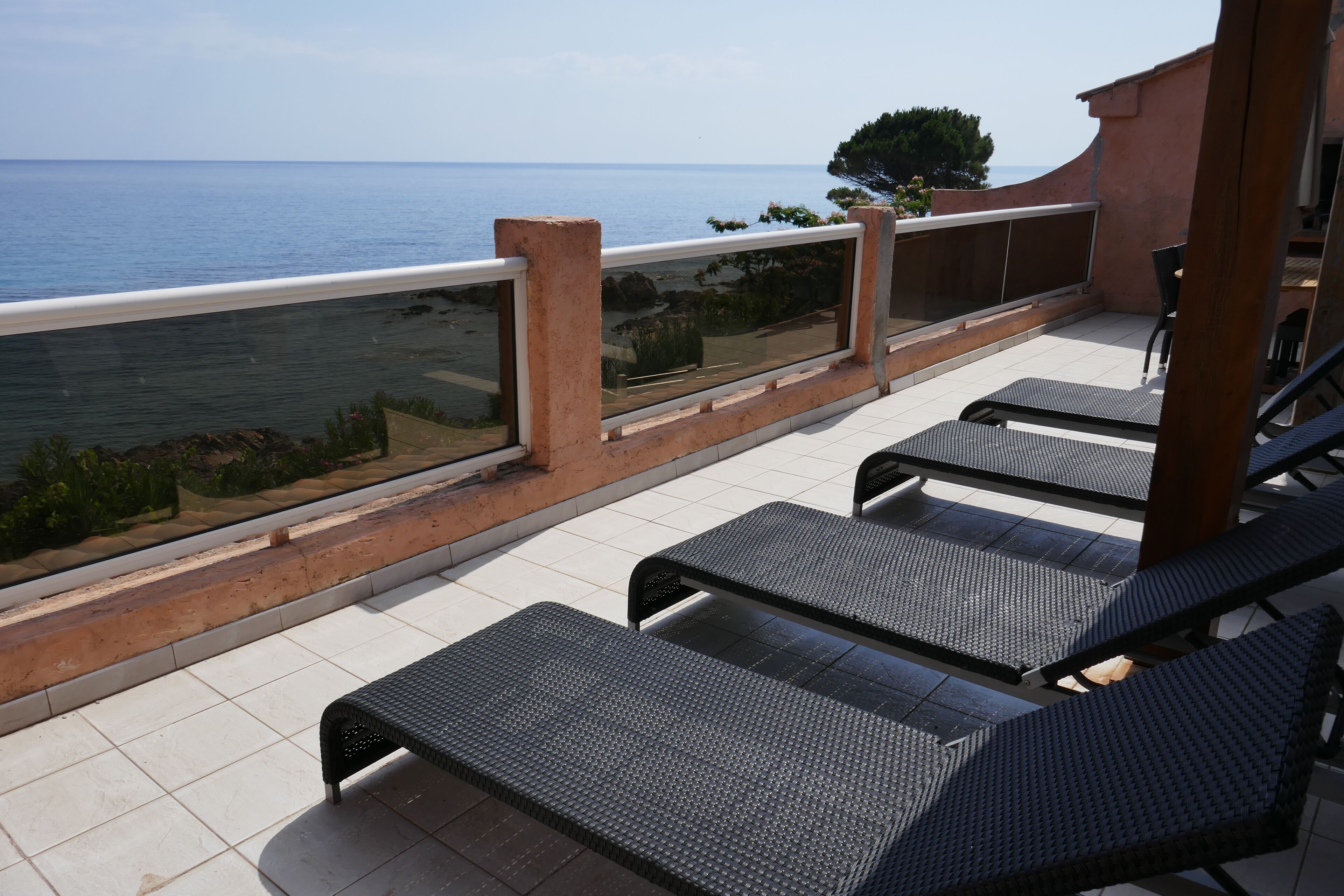 A balcony with a view of the sea, featuring a railing, a table, and two chairs.