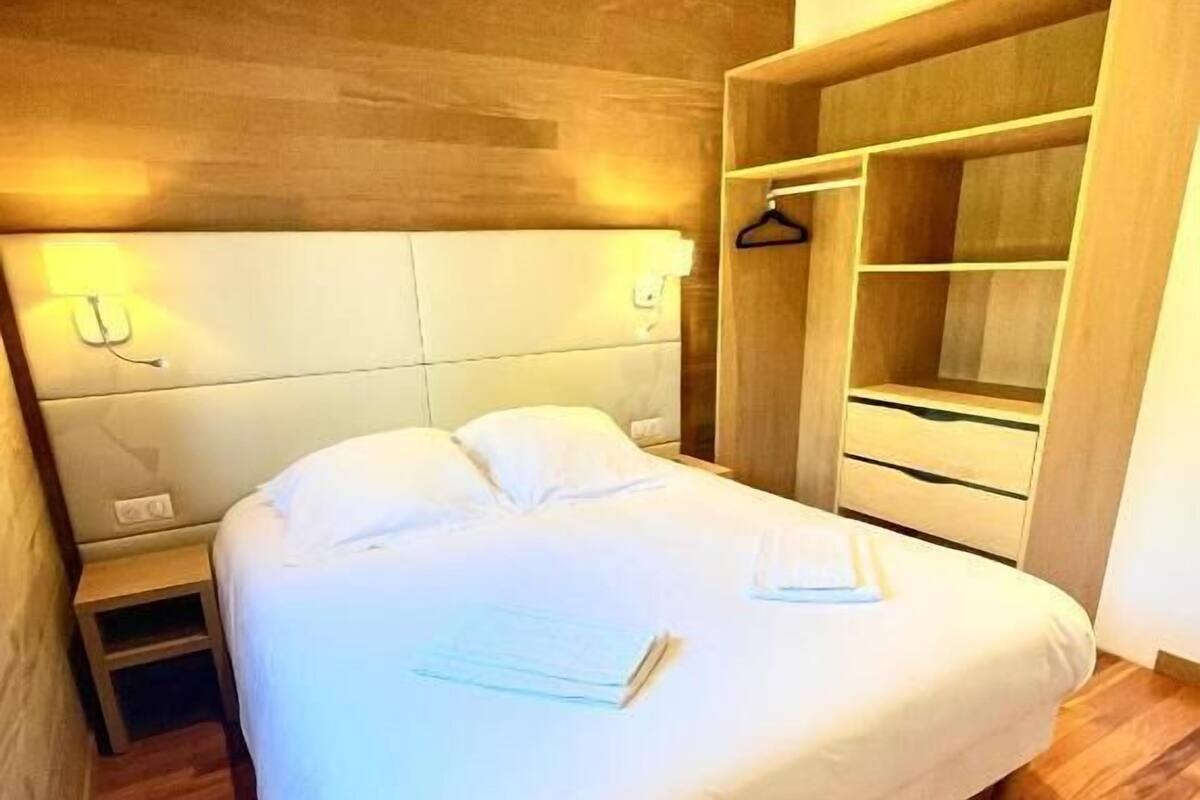 A neatly made bed in a room with wooden flooring and a built-in wardrobe.