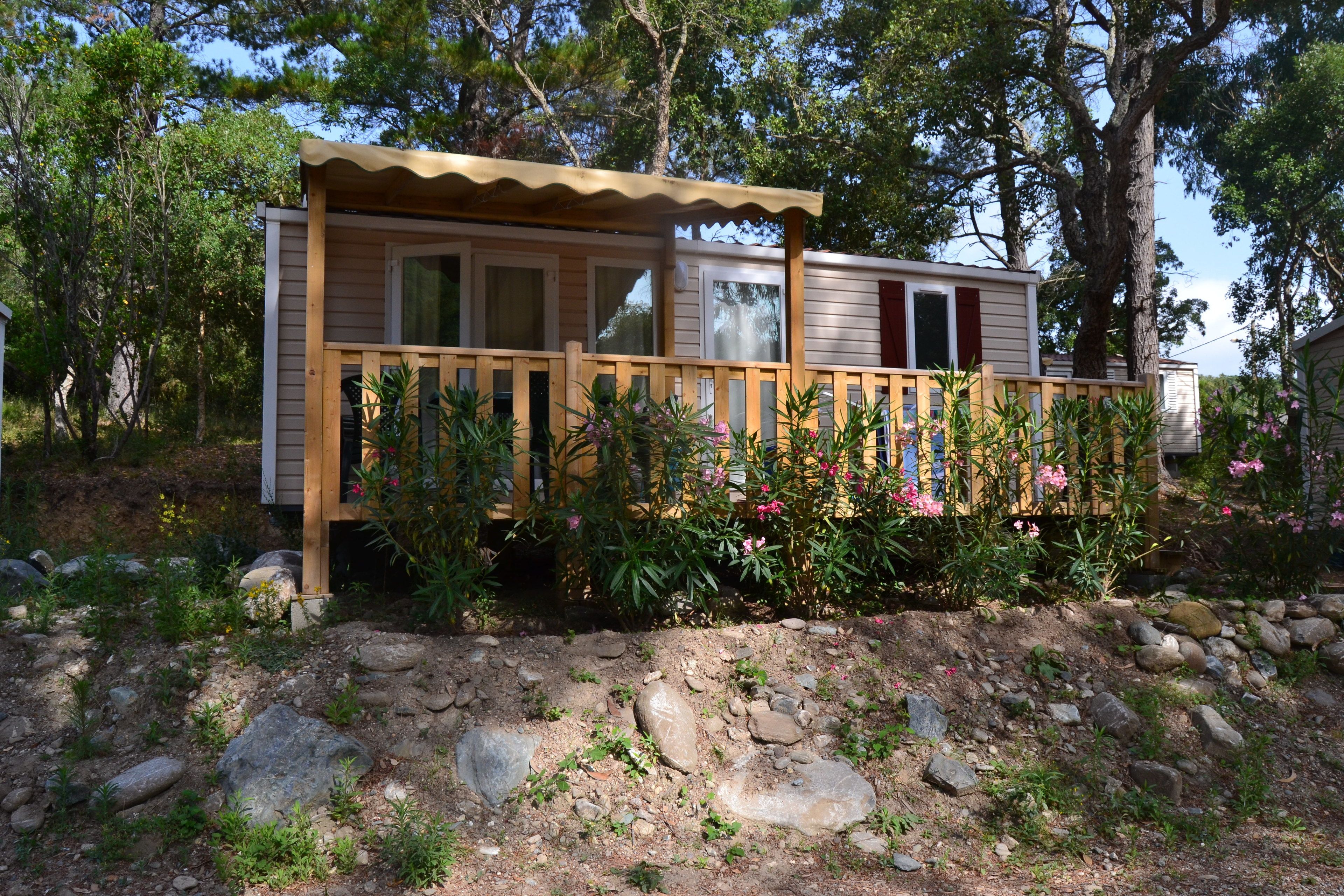 A wooden cabin with a deck, surrounded by rocks and plants.