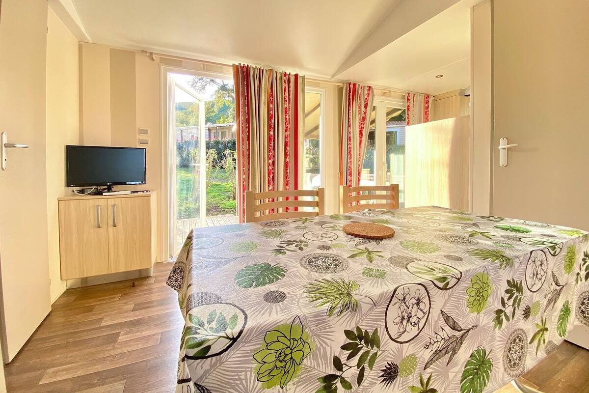 A bedroom with a bed, a TV on a wooden cabinet, and a sliding glass door to a garden.