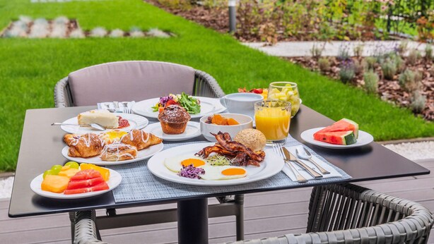 Una mesa de desayuno al aire libre con platos de comida, un vaso de jugo de naranja y una silla de mimbre.
