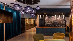Un área de bar moderna con un letrero de neón, lámparas esféricas reflectantes y asientos cómodos.