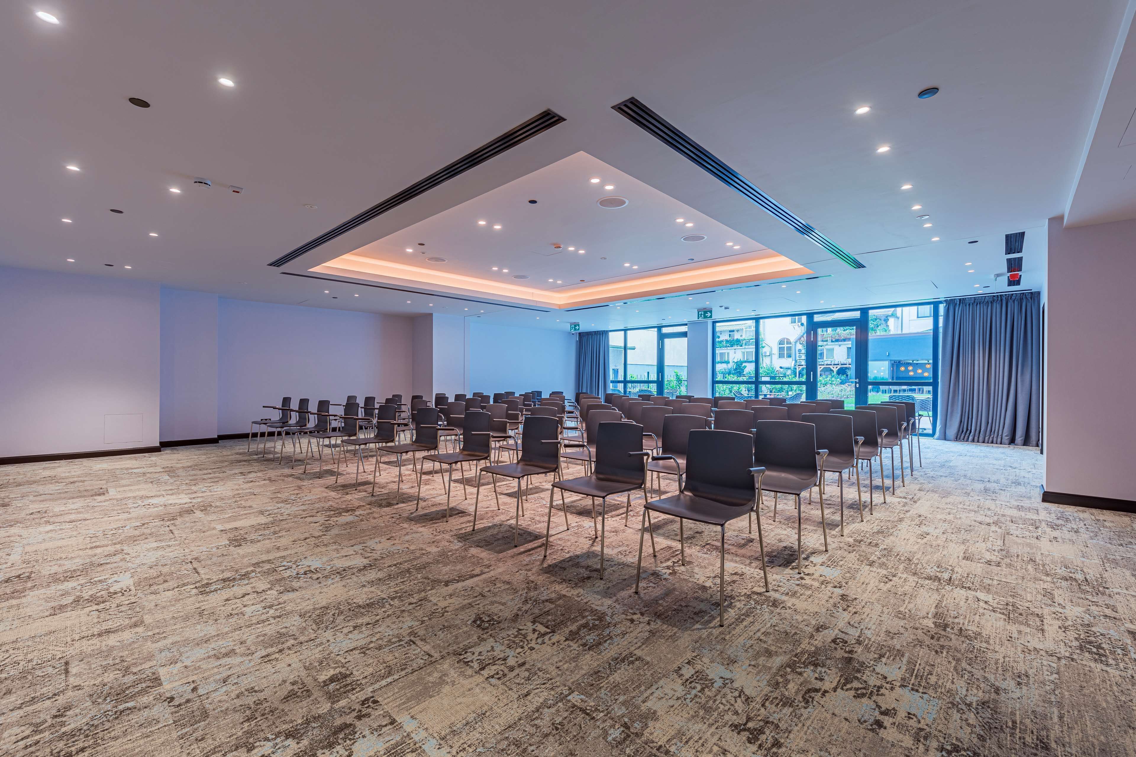 Een congreszaal met rijen stoelen, een vloerbedekking en een plafond met ingebouwde verlichting.