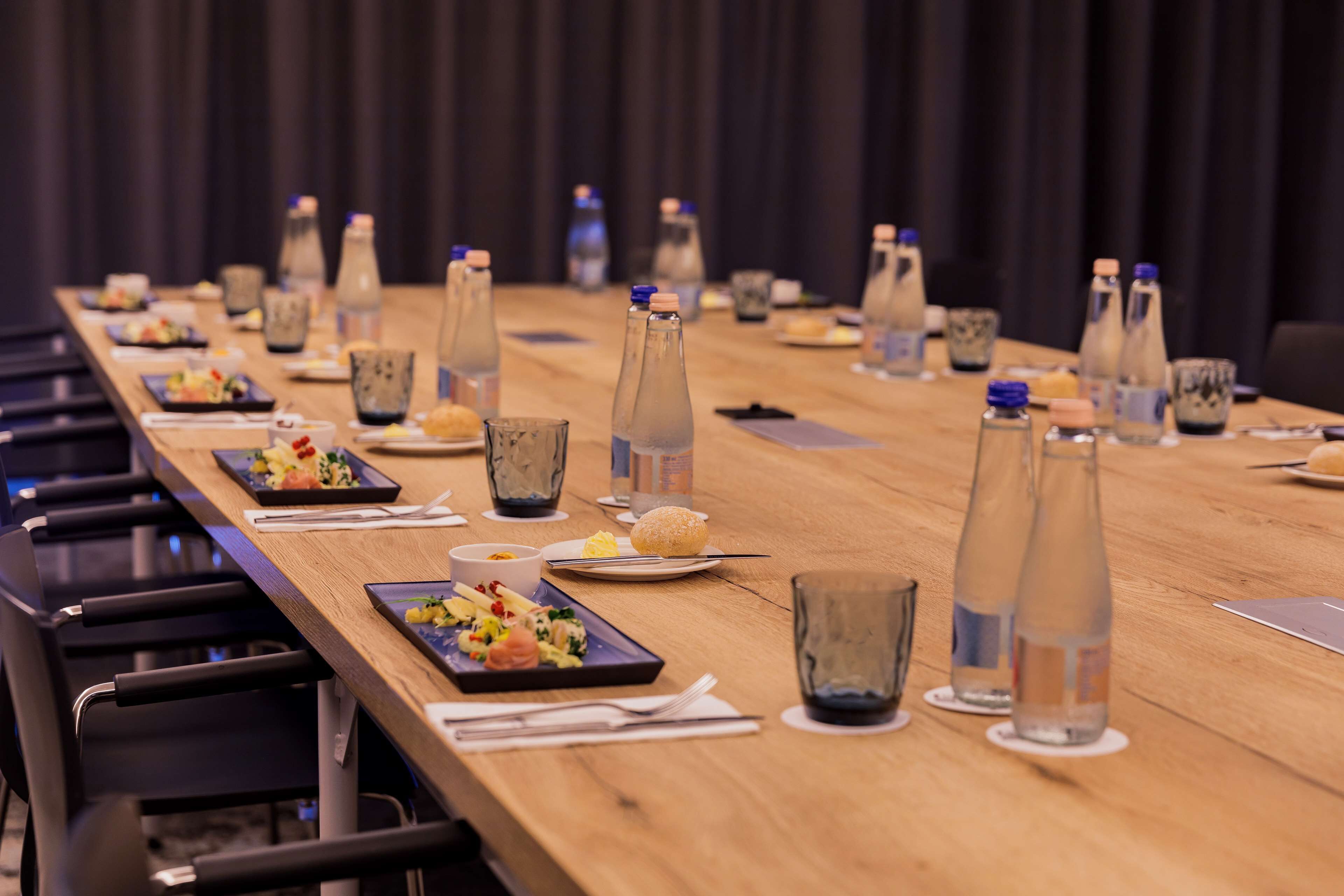 A long conference table set with plates of food, glasses, and water bottles.