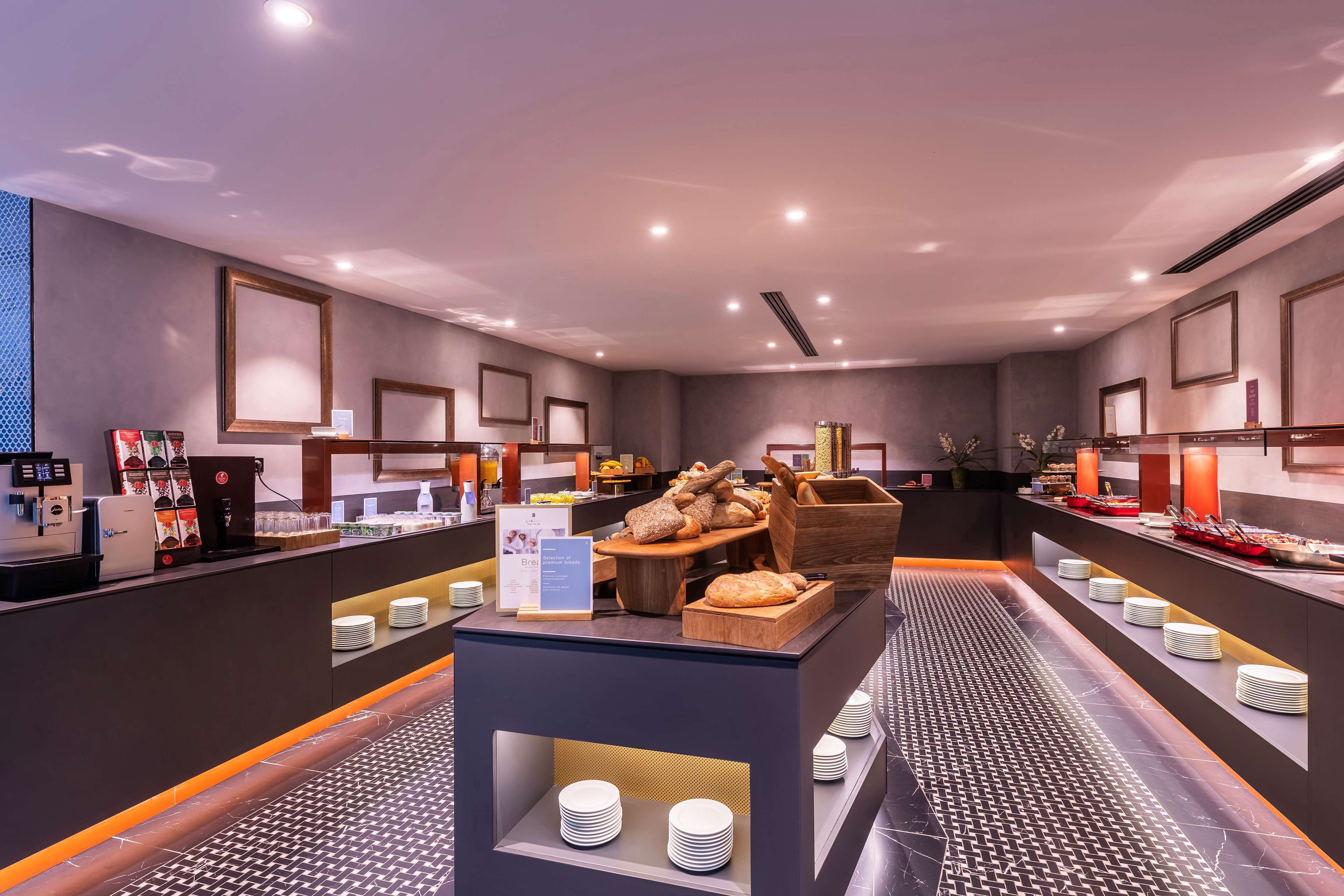 A modern breakfast area with a coffee machine, a variety of bread, and a fruit display.