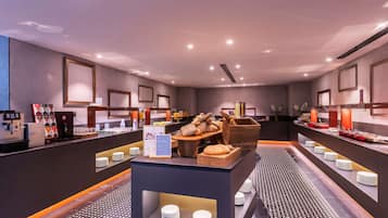 A modern breakfast area with a coffee machine, a variety of bread, and a fruit display.