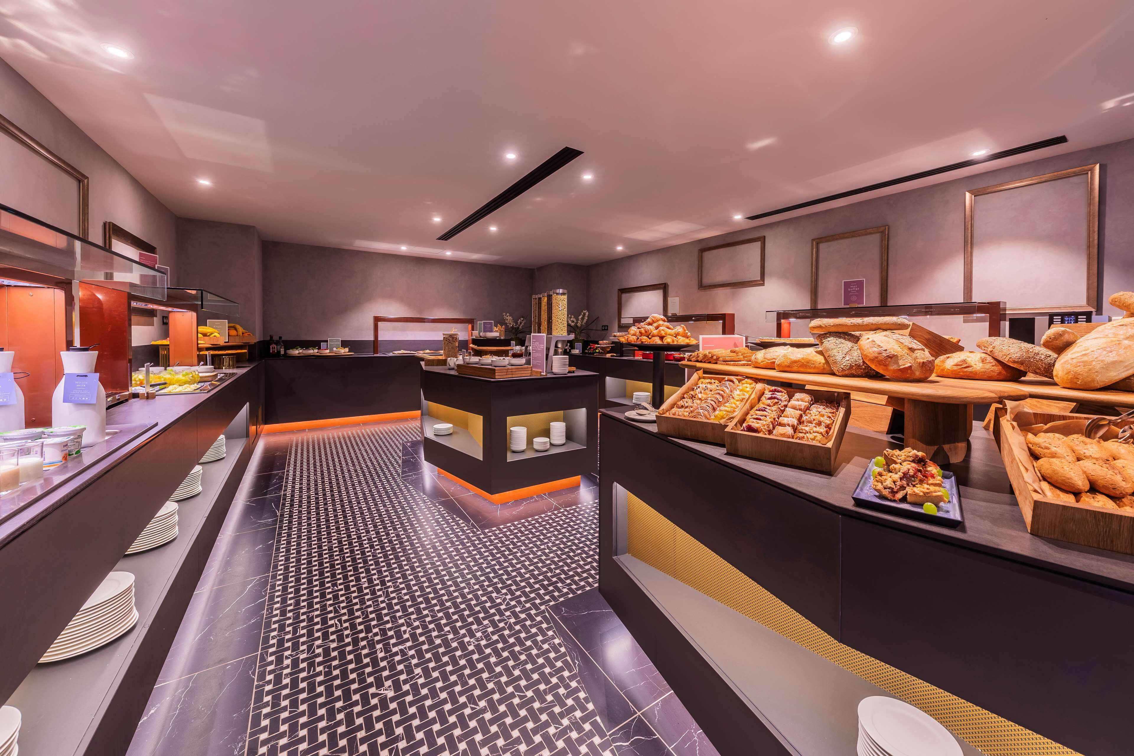 Un área de desayuno de hotel moderna con una variedad de pasteles y frutas.