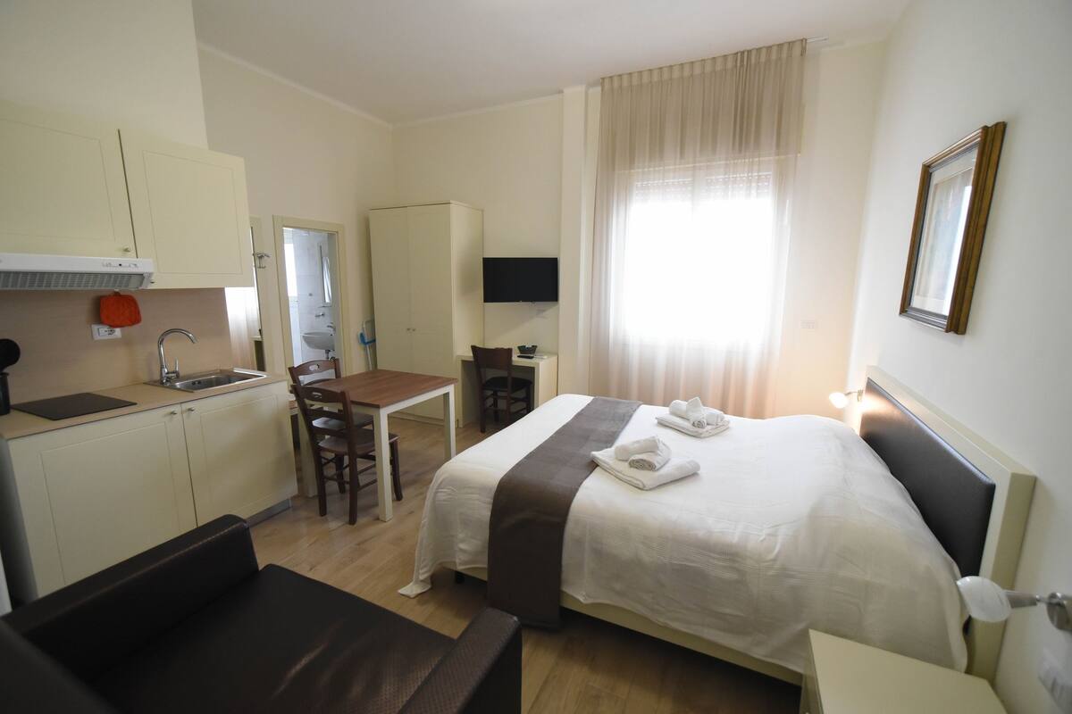 Una habitación de hotel con cama, escritorio, silla, televisor y kitchenette.