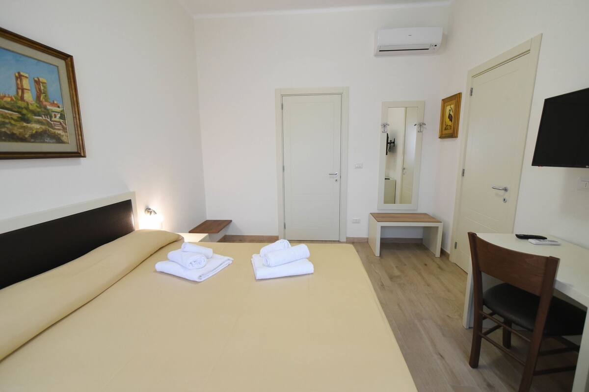 Una habitación de hotel con cama, escritorio, silla, televisor y puerta del baño.