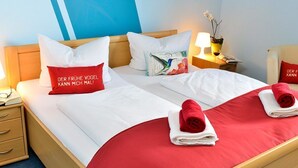 A hotel room with two beds, red and white bedding, and pillows with text. There are bedside tables with lamps and a nightstand with a lamp and a vase with flowers. - Ferienwohnung Panoramablick (Kastellaun)
