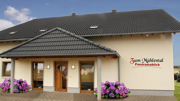 A two-story building with a tiled roof, a wooden front door, and a sign that reads "Zum Mühltal Panoramablick." - Ferienwohnung Panoramablick (Kastellaun)