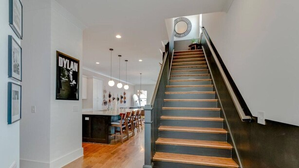 Un interior moderno con una escalera, piso de madera y una zona de cocina con lámparas colgantes.