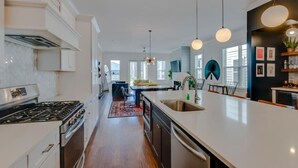 Una cocina moderna con una isla central, electrodomésticos de acero inoxidable, iluminación colgante y vistas al área de estar.