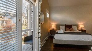 Habitación de hotel con una cama grande, dos mesitas de noche con lámparas, vista a través de una puerta corrediza y un espejo circular en la pared.