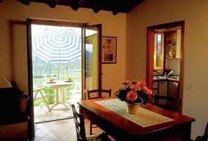 Comedor con una mesa dispuesta para dos personas, un florero y vistas a un área exterior con un paraguas a rayas.