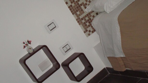 A bedroom with a bed, a small table with a vase, and a wall-mounted power outlet. - Verziere B&B (Jesi)