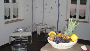 A dining area with a table and chairs, a fruit basket on a table, and a wall with a tree decal. - Verziere B&B (Jesi)
