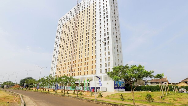 A tall, modern high-rise building with a grid-like facade, surrounded by a landscaped area with trees and a clear sky. - OYO 630 Green Lake View Cimanggis (Depok)