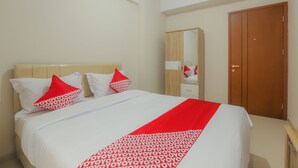A neatly made bed with white and red bedding, a wooden wardrobe, and a mirror on the wall. - OYO 630 Green Lake View Cimanggis (Depok)