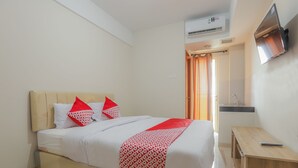 A neatly made bed with a patterned blanket and red pillows, a wooden nightstand, and a flat-screen TV mounted on the wall. - OYO 630 Green Lake View Cimanggis (Depok)