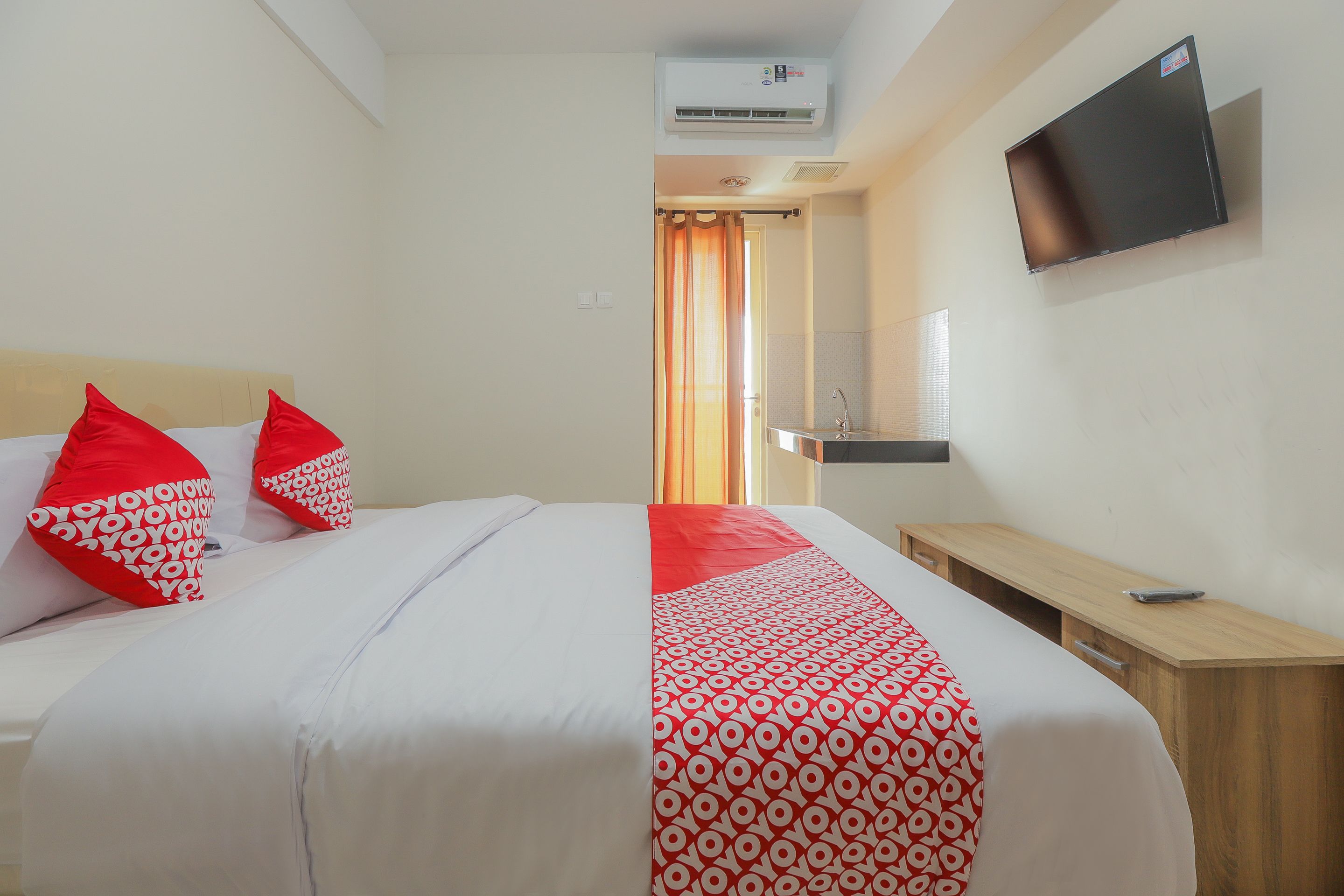 A hotel room with a bed, a TV mounted on the wall, and a wooden nightstand.